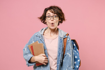 Naklejka premium Shocked young girl student in denim clothes glasses backpack isolated on pastel pink background. Education in high school university college concept. Mock up copy space. Hold books keeping mouth open.