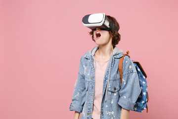 Shocked young woman student in denim clothes backpack posing isolated on pastel pink background in studio. Education in high school university college concept. Mock up copy space. Watching in headset.