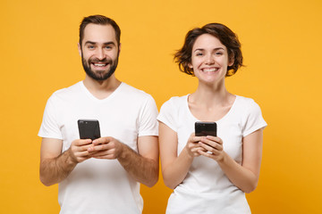 Smiling young couple friends bearded guy girl in white blank empty t-shirts isolated on yellow...