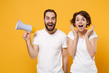 Cheerful young couple friends bearded guy girl in white blank empty t-shirts isolated on yellow...