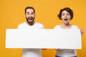 Surprised young couple friends bearded guy girl in white t-shirts isolated on yellow orange...