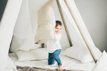 Small boy sitting in a teepee, having fun with the pillow.
