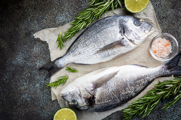 Fresh ready to cook raw bream fish dorado with ingredients and seasonings like rosemary, salt, pepper, lime and olive oil, top view
