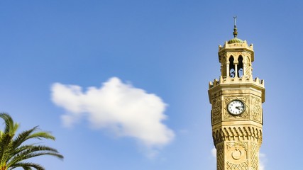Close-up of Izmir clock tower with palm tree and clouds.