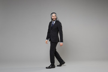 Smiling bearded young arabian muslim businessman in keffiyeh kafiya ring igal agal classic black suit shirt tie isolated on gray background. Achievement career wealth business concept. Looking aside.