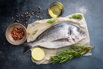 Fresh ready to cook raw bream fish dorado with ingredients and seasonings like rosemary, salt, pepper, lime and olive oil, top view