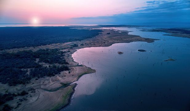 Aerial view of african lake Kariba and surrounding landscape in late evening with setting sun. Blue and pink colors. Dead trees in the water. Zimbabwe. Safari camping on the shore of lake Kariba.