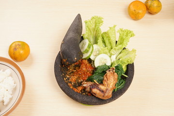 Vegetables, chili sauce, and fried chicken food above stone mortar and pestle