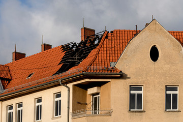 Destroyed roof framework after house fire with typical exterior wall facade, overcast, blue cloudy sky - concept real estate truss risk damage loss insurance abandoned building living condition