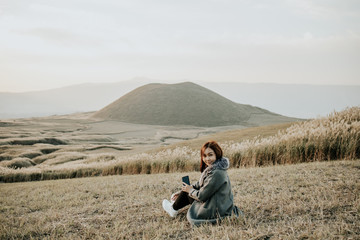Fototapeta na wymiar Lovely cute japanese girl sitting on Aso active volcano background with smoke at Mount Aso Nakadake, Kumamoto, kyushu, Japan (photo grain some noise for film colour)