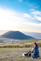 Lovely cute japanese girl sitting on Aso active volcano background with smoke at Mount Aso Nakadake, Kumamoto, kyushu, Japan (photo grain some noise for film colour)