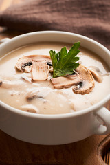 Bowl of mushroom soup with slices of chopped mushroom and napkin on a wooden table vertical frame