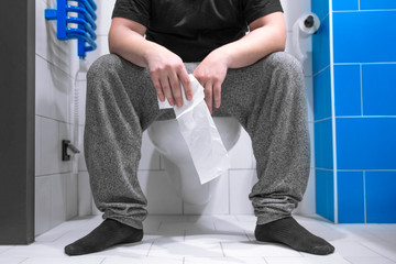 Man holding tissue roll in sitting on the toilet  bowl at home or hotel
