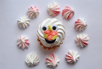 Cake with whipped cream and meringue. White, slightly grayish background. White green rose cream. Tartlet-shaped cake. Cake decorated with cream flowers and funny eyes.