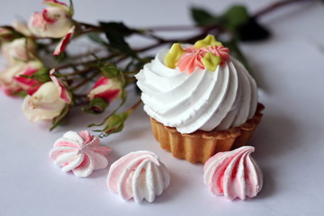 Cake with whipped cream and meringue. White, slightly grayish background. White green rose cream. Tartlet-shaped cake. Cake decorated with cream flowers 