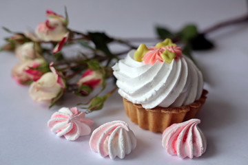 Cake with whipped cream and meringue. White, slightly grayish background. White green rose cream. Tartlet-shaped cake. Cake decorated with cream flowers 