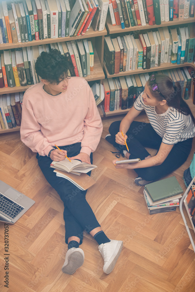 Poster two teenage classmates with books discussing passage from novel or story while preparing for class o