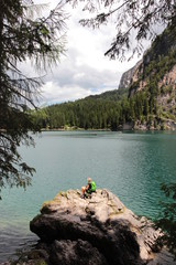 Figura pensierosa seduta su roccia davanti ad un lago