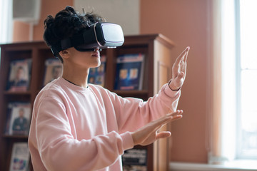 Mobile college student in casualwear and vr goggles touching virtual screen while moving in three...