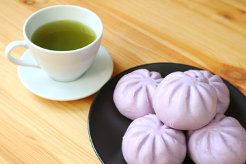 Plate of purple sweet potato steamed buns with blurry cup of green tea in the backdrop