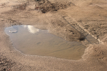 Transparent puddle on wet dirt road with dirty sand