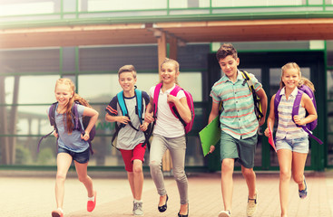 primary education, friendship, childhood and people concept - group of happy elementary school students with backpacks running outdoors