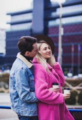 Happy couple with coffee during walk in city. Outdoor photo of happy young pair enjoying date