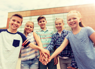 primary education, friendship, childhood and people concept - group of happy elementary school students with hands on top outdoors