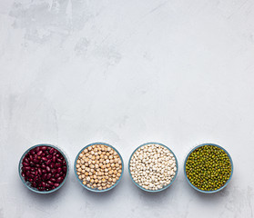 Bowls of various legumes: chickpeas, lentils, mung, red and white bean on a gray background.