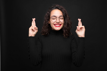 young pretty woman smiling and anxiously crossing both fingers, feeling worried and wishing or...