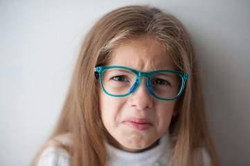 emotional sad caucasian little girl in blue glasses crying with bitter tear on her face with grimace of frustration