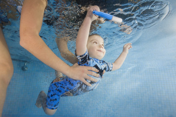 boy in a swimming suit Betman with toy dives underwater in a swimming pool, mother holding the child.