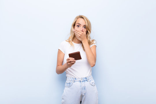 young blonde woman covering mouth with hands with a shocked, surprised expression, keeping a secret or saying oops holding a wallet