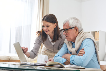 Young brunette woman pointing at laptop display while showing her senior father how to make online shopping