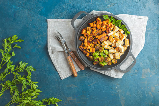 Healthy food. Pan of baking chicken meat, fried sweet potato and brussels sprouts. Top view, classic blue concrete surface, flat lay. Color of 2020 year. Classic Blue, food trendy background