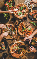 Friends having pizza party dinner. Flat-lay of people eating different kinds of Italian pizza, salad and drinking red wine over wooden table, top view. Fast food lunch, gathering, celebration - 320745210