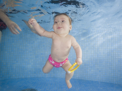 Little baby with toy learning to swim underwater in a swimming pool