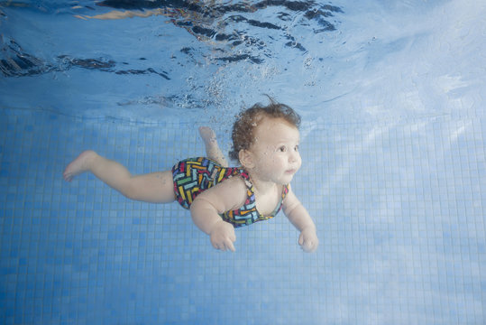 Little baby in a swimsuit learning to swim underwater in a swimming pool