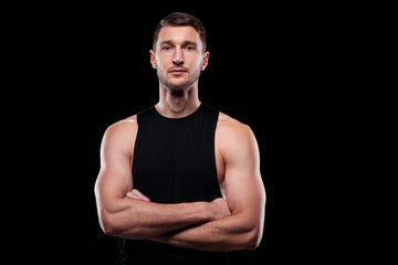 Fototapeta premium Young muscular athlete in black vest crossing his arms by chest while standing in front of camera in isolation