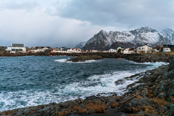 Panorama of Henningsvaer village with sea shore, colorful buildings and mountain on horizon.