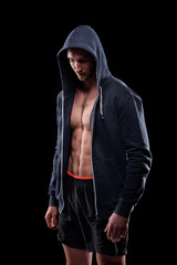 Obraz na płótnie Canvas Young athlete in shorts and unzipped hoodie standing in front of camera in isolation over black background