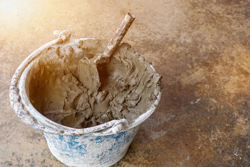 Closeup wood trowel for building construction with mortar cement in bucket at construction site on sun flare background.