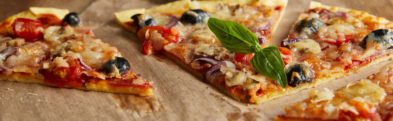 cut delicious italian pizza with olives and basil on baking paper on wooden table, panoramic shot