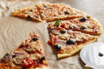 close up view of cut delicious italian pizza with olives on baking paper with pizza knife on wooden table