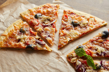 cut delicious italian pizza with olives on baking paper on wooden table