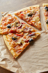 cut delicious italian pizza with olives on baking paper on wooden background