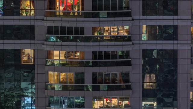 Night view of exterior apartment building timelapse. High rise skyscraper with blinking lights in windows with people moving inside. Zoom out