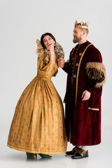 smiling queen and king with crowns holding hands on grey background