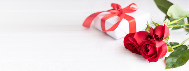 Red roses bouquet and white gift box with red ribbon bow. Giving present concept.Large festive background for banner