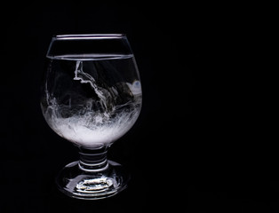 Glass filled with water and paint spilling inside, on a black background